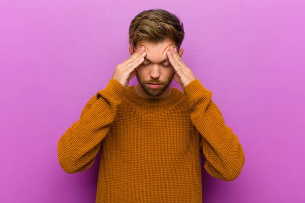 young man looking stressed and frustrated, working under pressure with a headache and troubled with problems against purple background