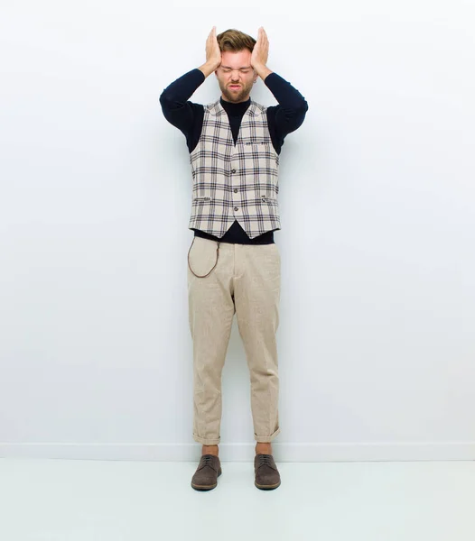 young full body man feeling stressed and anxious, depressed and frustrated with a headache, raising both hands to head against white background