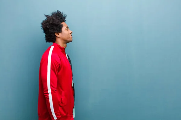 young black sports man on profile view looking to copy space ahead, thinking, imagining or daydreaming against grunge wall