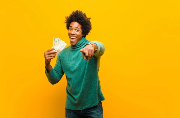 Jonge Afro-Amerikaanse man met dollarbiljetten tegen oranje rug — Stockfoto