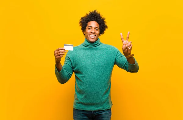 Joven afroamericano hombre con una tarjeta de crédito contra bac naranja — Foto de Stock