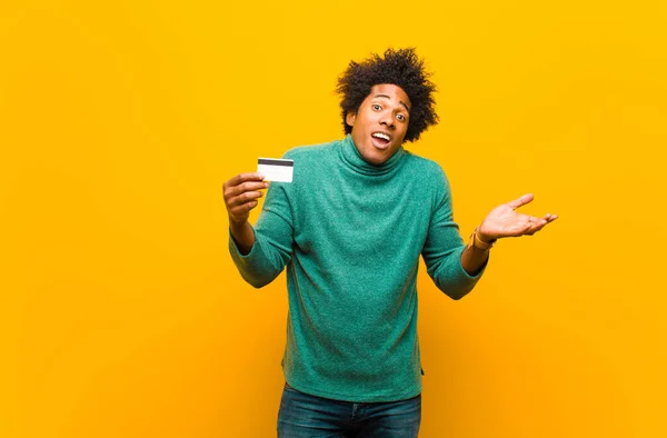 Молодой африканский американец с кредитной картой против оранжевого цвета — стоковое фото