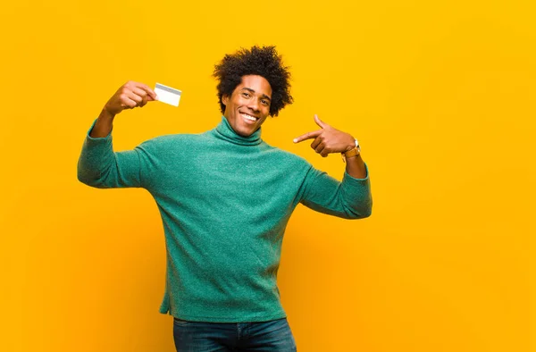 Young african american man with a credit card against orange bac — Stock Photo, Image