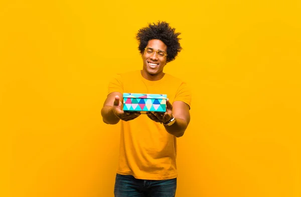 Молодой африканский американец с подарочной коробкой против оранжевого backgr — стоковое фото