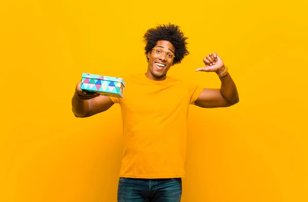 Jong Afrikaans amerikaans man met een gift box tegen oranje backgr — Stockfoto