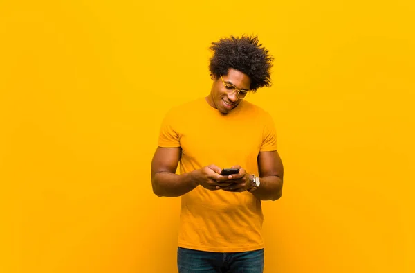 Joven afroamericano hombre con un teléfono inteligente contra naranja bac — Foto de Stock