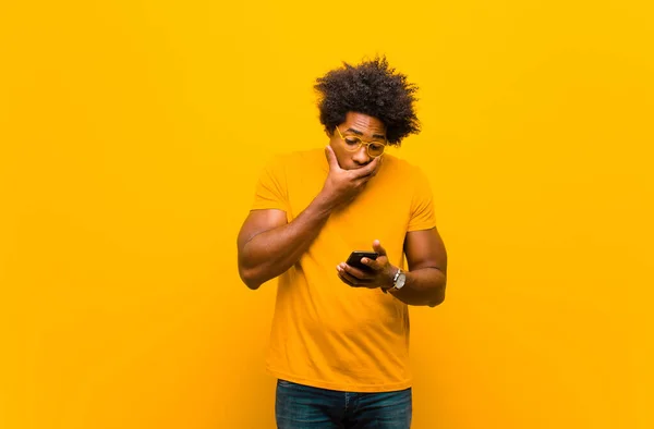 Young african american man with a smart phone against orange bac — ストック写真