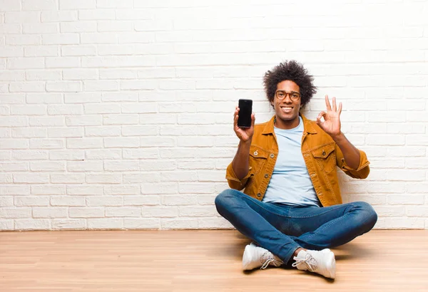 Jeune homme noir avec un téléphone intelligent assis sur le sol — Photo