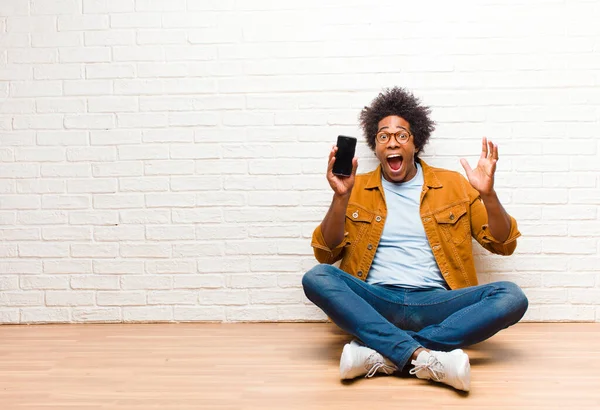 Joven hombre negro con un teléfono inteligente sentado en el suelo —  Fotos de Stock