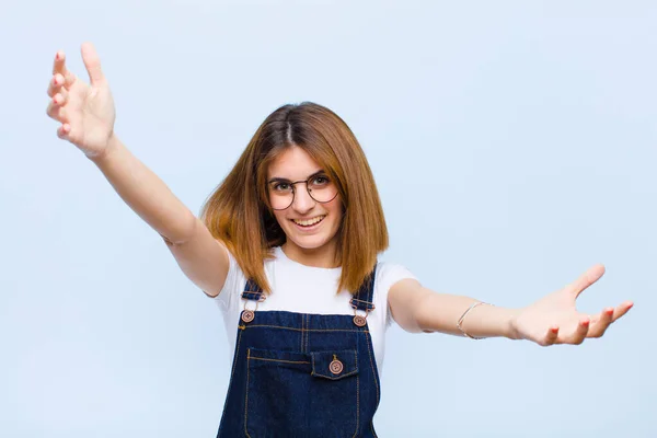 young pretty woman smiling cheerfully giving a warm, friendly, loving welcome hug, feeling happy and adorable against blue background