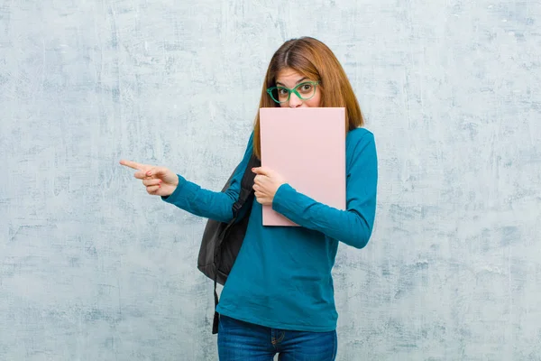 若い学生の女性は幸せ ショックと驚きを感じ 手で口を覆い グランジの壁の背景に対して横方向のコピースペースを指す — ストック写真