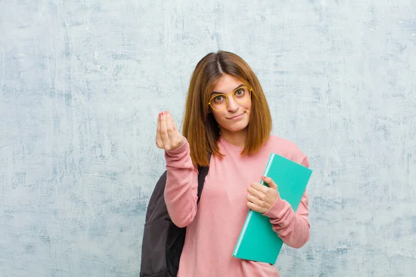 young student woman making capice or money gesture, telling you to pay your debts! against grunge wall background