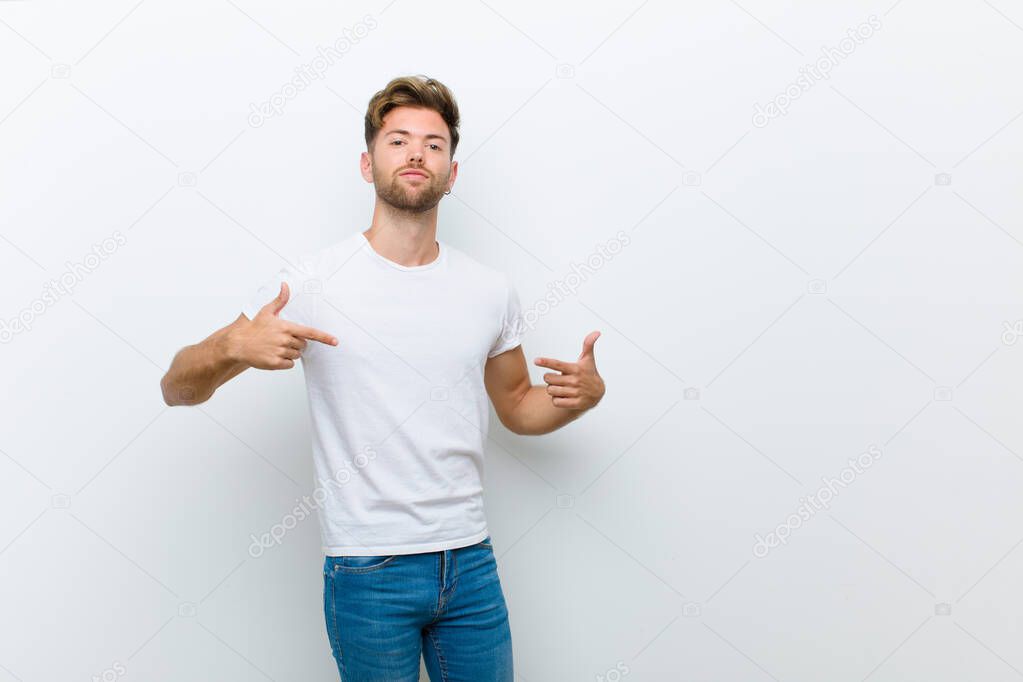young man looking proud, arrogant, happy, surprised and satisfied, pointing to self, feeling like a winner against white background