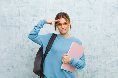 Genç bir bayan öğrenci kamerayı selamlıyor onur ve vatanseverlik eylemiyle, grunge wall arka planına saygı göstererek.