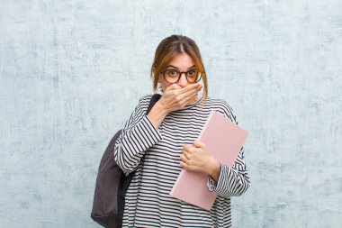 Elleriyle ağzını kapatan genç bir bayan öğrenci şok olmuş, şaşırmış bir ifadeyle, bir sır saklıyor ya da grunge Wall arka planına karşı 