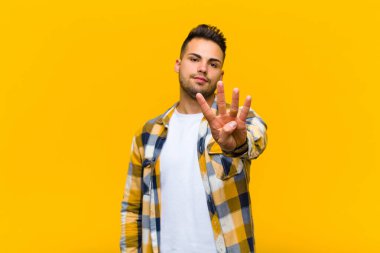 Genç İspanyol adam gülümsüyor ve dost canlısı görünüyor. Elleri önde, turuncu duvara doğru sayıyor.