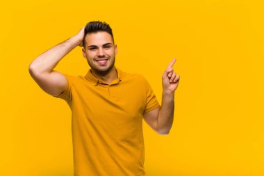 Genç İspanyol adam gülüyor, mutlu, pozitif ve şaşırmış görünüyor, turuncu duvara karşı yanal fotokopi alanını gösteren harika bir fikrin farkına varıyor.