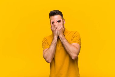 Genç İspanyol adam korkmuş ya da utanmış hissediyor, gözleri yarı kapalı turuncu duvara bakıyor ya da dikizliyor.