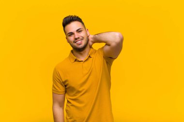 Genç İspanyol adam turuncu duvarın karşısında neşeli, mutlu, dostane bir gülümsemeyle güler.