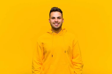 Genç İspanyol adam mutlu ve hoş bir şekilde şaşırmış görünüyor, turuncu duvarın karşısında büyüleyici ve şok olmuş bir ifadeyle heyecanlanıyor.