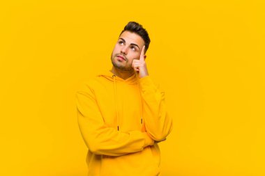 Yoğunlaşmış bakışları olan genç İspanyol bir adam şüpheli bir ifadeyle turuncu duvara bakıp duruyor.