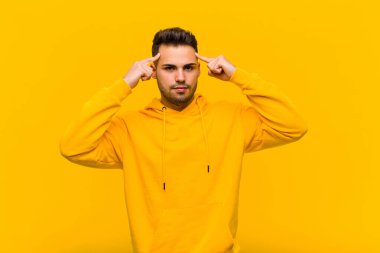 Ciddi ve konsantre bakışlı genç İspanyol adam, turuncu duvara karşı zorlu bir sorun düşünüyor ve beyin fırtınası yapıyor.