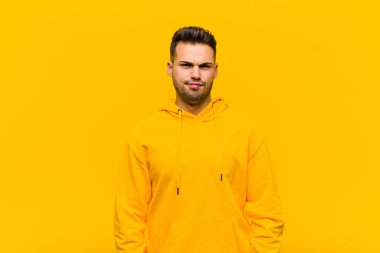 Genç İspanyol adam şaşkın ve kuşkulu hissediyor, merak ediyor ya da turuncu duvara karşı karar vermeye çalışıyor.