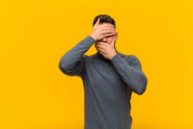 Genç İspanyol adam kameraya hayır diyen iki eliyle yüzünü kapatıyor! Resimleri reddetmek ya da turuncu duvara karşı fotoğraf yasaklamak