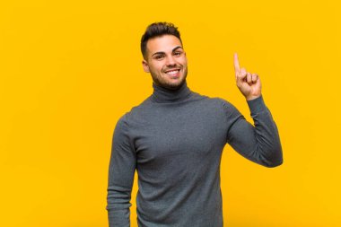 Genç İspanyol bir adam bir fikri fark ettikten sonra mutlu ve heyecanlı bir dahi gibi hissediyor. Neşeli bir şekilde parmağını kaldırıyor. Evreka! turuncu duvara yaslan
