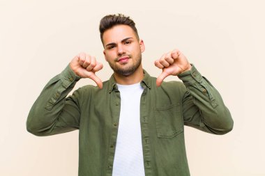 Genç Hispanik adam üzgün, hayal kırıklığına uğramış ya da kızgın görünüyor, anlaşmazlık içinde parmaklarını gösteriyor, izole edilmiş arka plana karşı hayal kırıklığına uğramış hissediyor