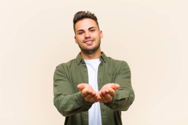 Genç İspanyol adam mutlu bir şekilde gülümsüyor, arkadaş canlısı, kendine güvenen, olumlu bakışlı, izole edilmiş arka plana karşı bir nesne ya da konsept sunuyor ve gösteriyor.