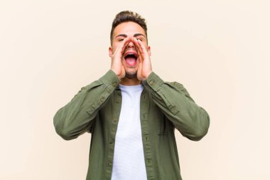 Genç İspanyol adam mutlu, heyecanlı ve pozitif hissediyor, elleri ağızının yanında bağırıyor, izole edilmiş arka plana bağırıyor.