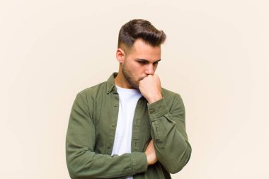 Genç İspanyol bir adam ciddi, düşünceli ve endişeli, elleri çenesine bastırılmış, izole edilmiş arka planda.