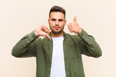 Genç İspanyol adam kafası karışık, bilgisiz ve kararsız hissediyor, iyi ve kötü seçenekleri farklı seçeneklerle tartıyor veya izole edilmiş arka planla karşılaştırıyor.