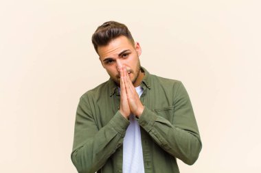 Genç İspanyol bir adam endişeli, umutlu ve dindar hissediyor, avuçlarıyla inançla dua ediyor, soyutlanmış arka plana karşı af diliyor.