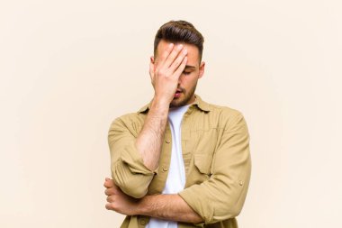 Genç İspanyol bir adam stresli, utanmış ya da üzgün görünüyor, baş ağrısı var, yüzünü kapalı bir arka planda tutuyor.
