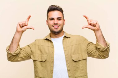 Genç İspanyol asıllı bir adam kendi gülüşünü çiziyor, iki eliyle, pozitif ve mutlu görünüyor, izole edilmiş arka plana karşı sağIık kavramı