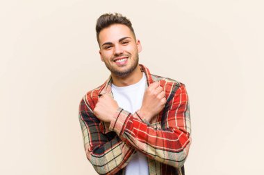 Genç İspanyol adam sevinçle gülümsüyor ve kutluyor, yumruklarını sımsıkı kavrayıp kollarını kavuşturuyor, izole edilmiş arka planda mutlu ve pozitif hissediyor.
