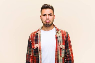 Genç İspanyol bir adam üzgün ve stresli hissediyor, kötü bir sürpriz yüzünden üzgün, izole edilmiş arka plana karşı olumsuz, endişeli bir bakışla