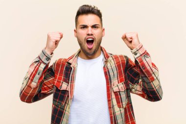 Genç İspanyol bir adam öfkeli bir ifadeyle agresif bir şekilde bağırıyor ya da izole edilmiş arka plana karşı başarıyı kutlayan yumruklarla.