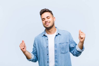 Genç İspanyol adam gülümsüyor, kaygısız, rahat ve mutlu hissediyor, dans ediyor ve müzik dinliyor, mavi duvara karşı bir partide eğleniyor.