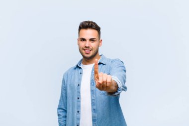 İspanyol asıllı genç adam gururla gülümsüyor ve gururla bir numaralı pozu veriyor. Mavi duvara karşı bir lider gibi hissediyor.