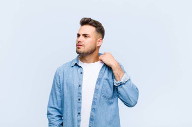 Genç İspanyol bir adam stresli, endişeli, yorgun ve hayal kırıklığına uğramış, gömleğini çekmiş, mavi duvara karşı sorunlu görünüyor.