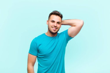 Genç İspanyol adam neşeli ve kendinden emin bir şekilde gülüyor mavi arka planda gülen, mutlu, dostane bir gülümsemeyle.