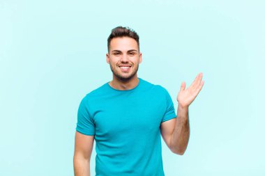 Genç İspanyol adam mutlu, şaşırmış ve neşeli hissediyor, pozitif bir tavırla gülümsüyor, mavi arka plana karşı bir çözüm ya da fikir buluyor.