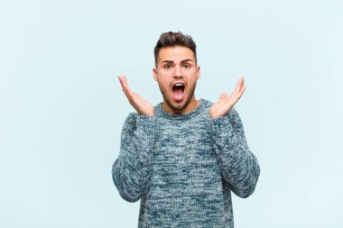 Genç İspanyol adam şok olmuş ve heyecanlı, gülüyor, şaşkın ve mutlu çünkü beklenmedik bir sürpriz mavi arka plana karşı