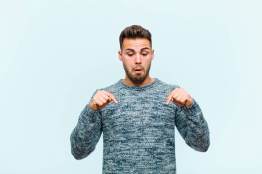 Genç İspanyol adam şoke olmuş, ağzı açık ve şaşırmış hissediyor. Mavi arka plana karşı inançsızlık ve şaşkınlık içinde bakıyor ve işaret ediyor.