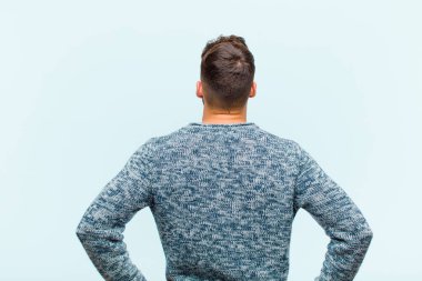 Genç İspanyol adamın kafası karışık ya da dolu ya da şüphe ve soru dolu, merak ediyorum, elleri kalçasında, mavi arka planda dikiz manzaralı