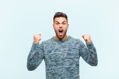 Genç İspanyol bir adam öfkeli bir ifadeyle ya da mavi arka plana karşı başarıyı kutlayan yumruklarla agresif bir şekilde bağırıyor.