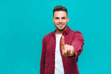 İspanyol asıllı genç adam gururla gülümsüyor ve gururla bir numaralı pozu veriyor. Mavi arka plana karşı bir lider gibi hissediyor.